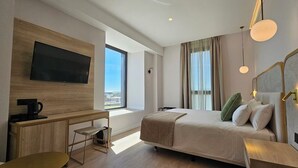 Una moderna camera d'albergo con un letto grande, una scrivania con una TV, una macchina per il caffè e vista sulla città.
