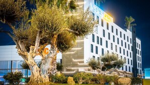 Un hotel moderno con un'insegna ben visibile che riporta 'VIBE'S', immerso in un paesaggio curato con alberi e arbusti.
