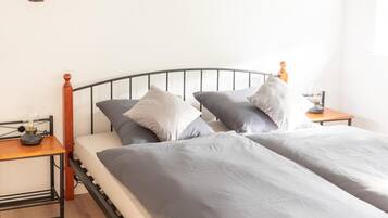 Ein Bett mit grauer Bettwäsche, einem Holzkopfende und zwei Nachttischen mit Lampen.