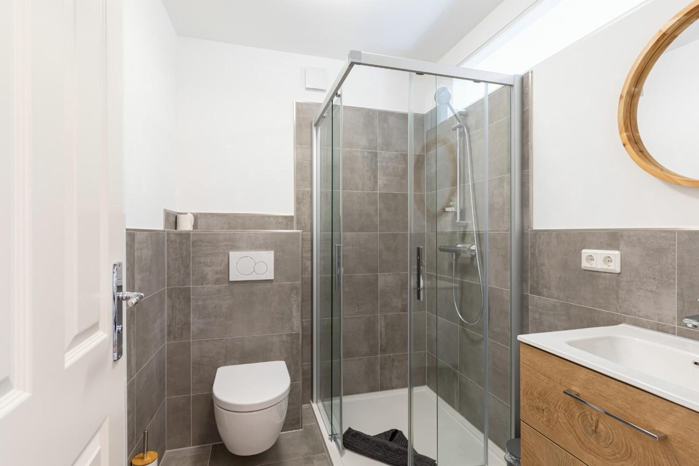 Une salle de bain moderne avec une douche à parois de verre, des toilettes blanches et un meuble-lavabo en bois avec un évier.