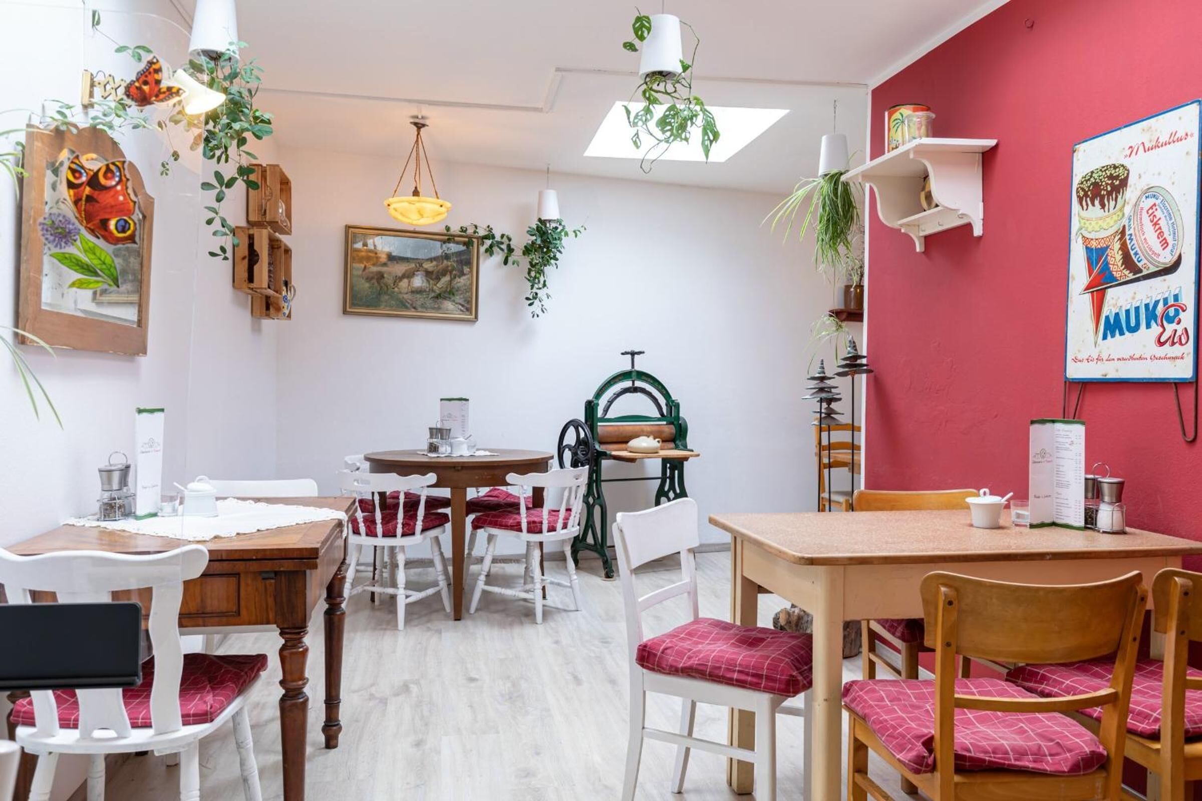 Un espace repas avec des tables et des chaises en bois, une chaise en métal vert et une étagère murale agrémentée d’une plante.