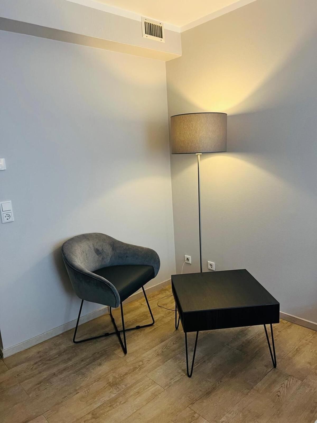 A modern room with a grey upholstered chair, a black square table, and a floor lamp.