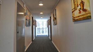 A hallway with a carpeted floor, recessed lighting, and artwork on the walls. - Hotel B99 (Offenbach am Main)