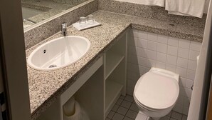 A modern bathroom with a granite countertop sink, a mirror, a toilet, and towel dispensers. - Hotel B99 (Offenbach am Main)