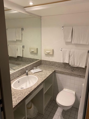 A modern bathroom with a granite countertop sink, a mirror, a toilet, and towel dispensers. - Hotel B99 (Offenbach am Main)