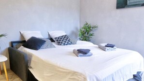 A modern bedroom with a bed, pillows, a small table, and a potted plant. - Appart Hotel Cholet Carteron (Cholet)
