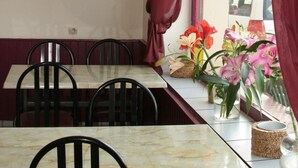 A dining area with a marble table and chairs, red curtains, and a window with flowers. - Hotel de L'avenue (Bonson)