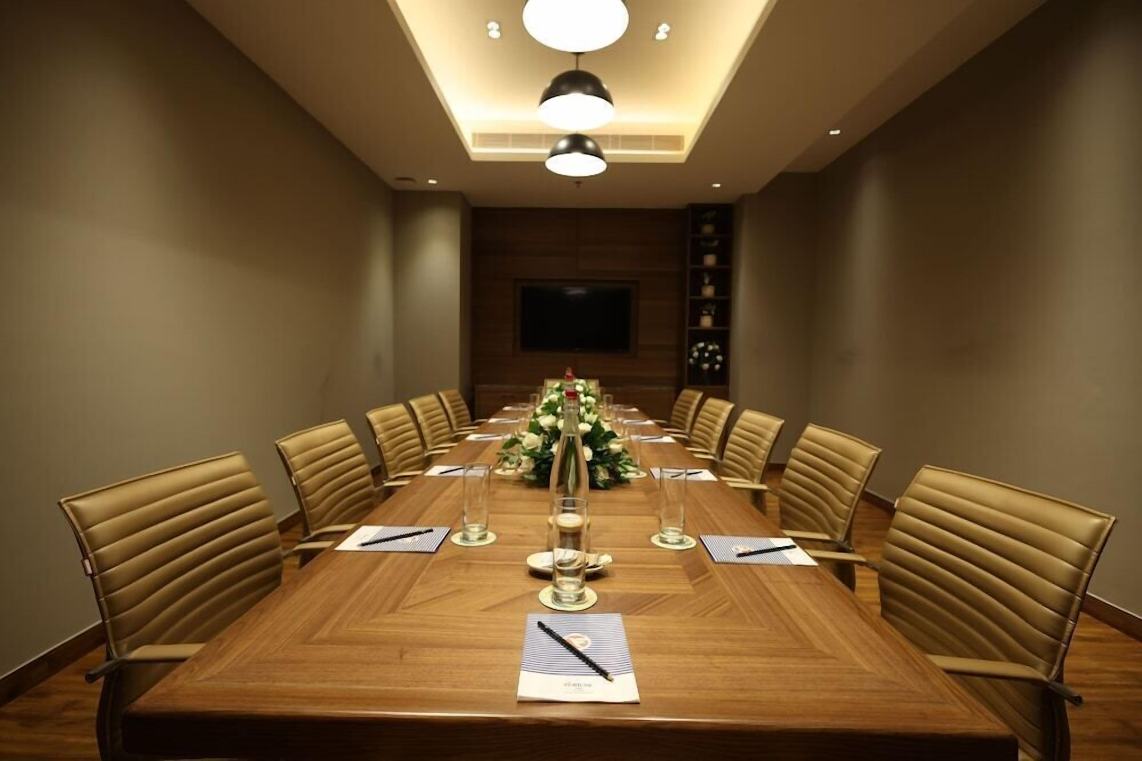 A conference room with a long table, chairs, a floral centerpiece, and a television on the wall.