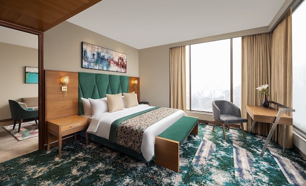 A hotel room with a large bed, a desk, a chair, and a view of the city. - Fortune Park East Delhi (New Delhi)