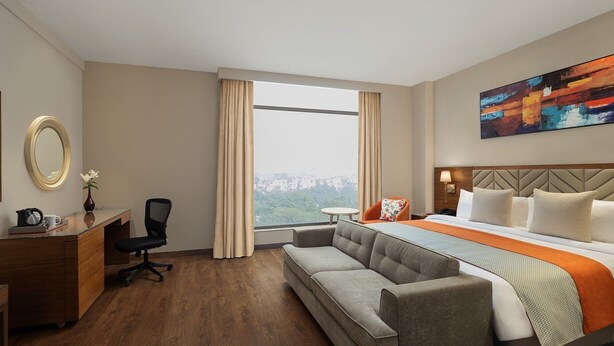 Hotelkamer met een bed, een slaapbank, een bureau, een stoel, een spiegel en een raam met uitzicht op de stad.