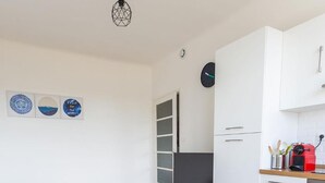 A modern kitchen with white cabinets, a built-in oven, and a microwave. There is a bench with a flat-screen TV, and a clock on the wall. - Apparthotel T3 Epicservices Saint-charles (Marseille)