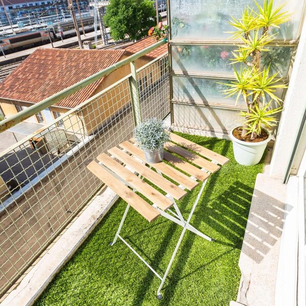 Ein Balkon mit Kunstgrastrittichkeit, einer Holzbank, einem Blumentopf und Blick auf die Stadtlandschaft.