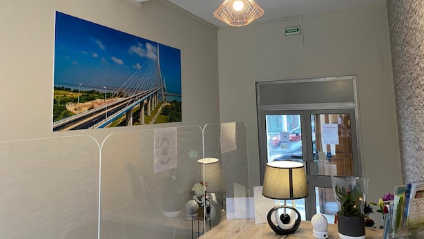 A hotel lobby with a large painting of a bridge, a modern lamp, and a reception desk with a plant. - Hotel De Normandie (Gournay-en-Bray)