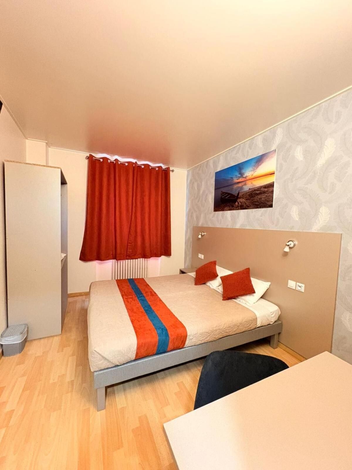 A bedroom with a bed, a desk, a wardrobe, and a window with curtains.