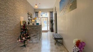 A hallway with a stone wall, a decorated Christmas tree, a bench, and a door leading to another room. - Hotel De Normandie (Gournay-en-Bray)