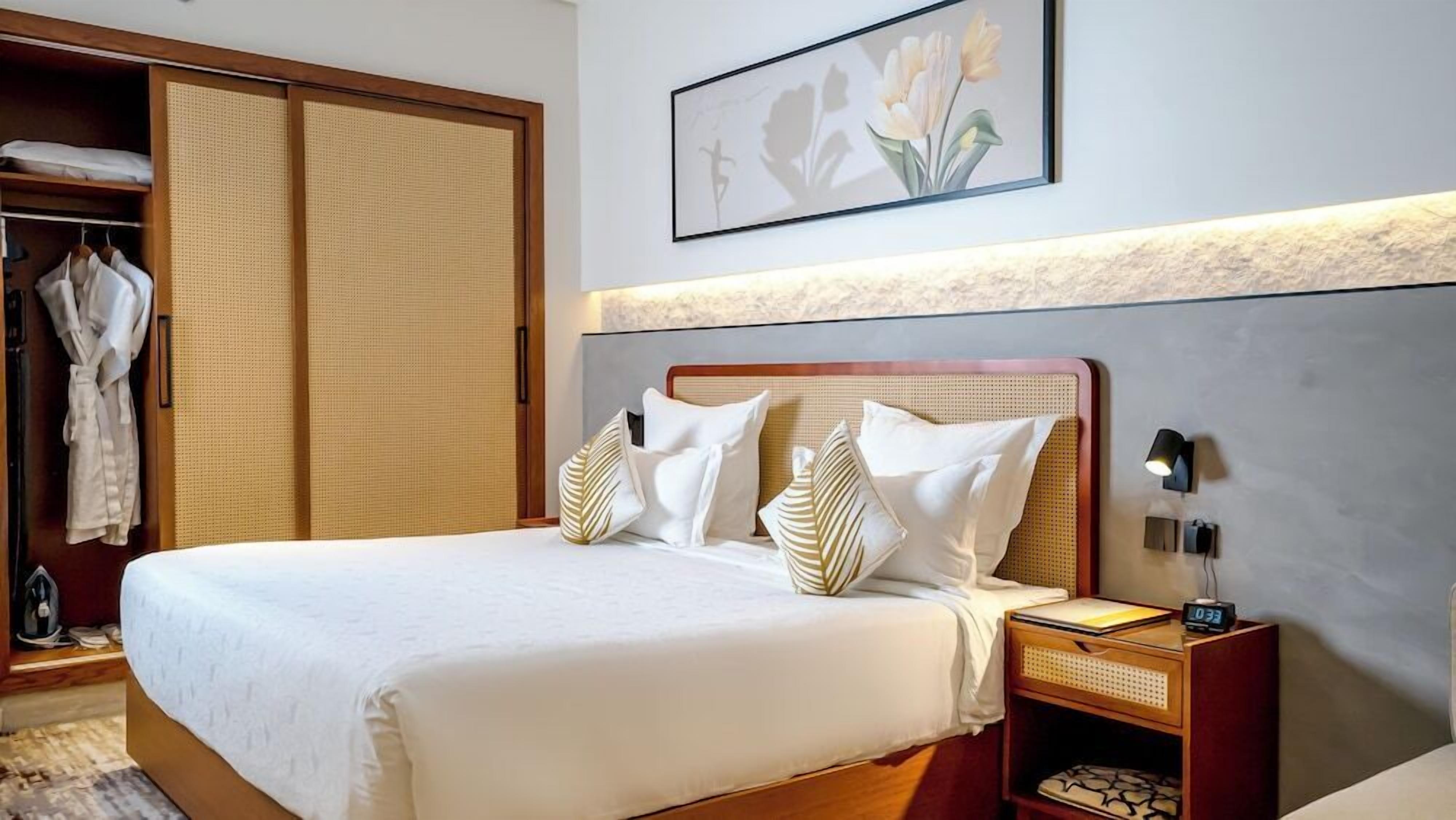 Ein Hotelzimmer mit Bett, Schrank, Nachttisch und einer Wandlampe.