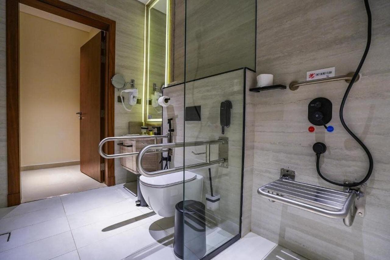 Un baño moderno con cabina de ducha de vidrio, inodoro, secador de manos y dispensador de jabón.