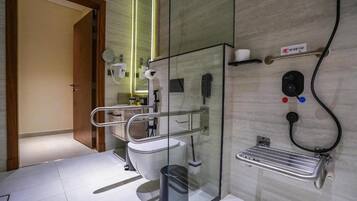 Un baño moderno con cabina de ducha de vidrio, inodoro, secador de manos y dispensador de jabón.