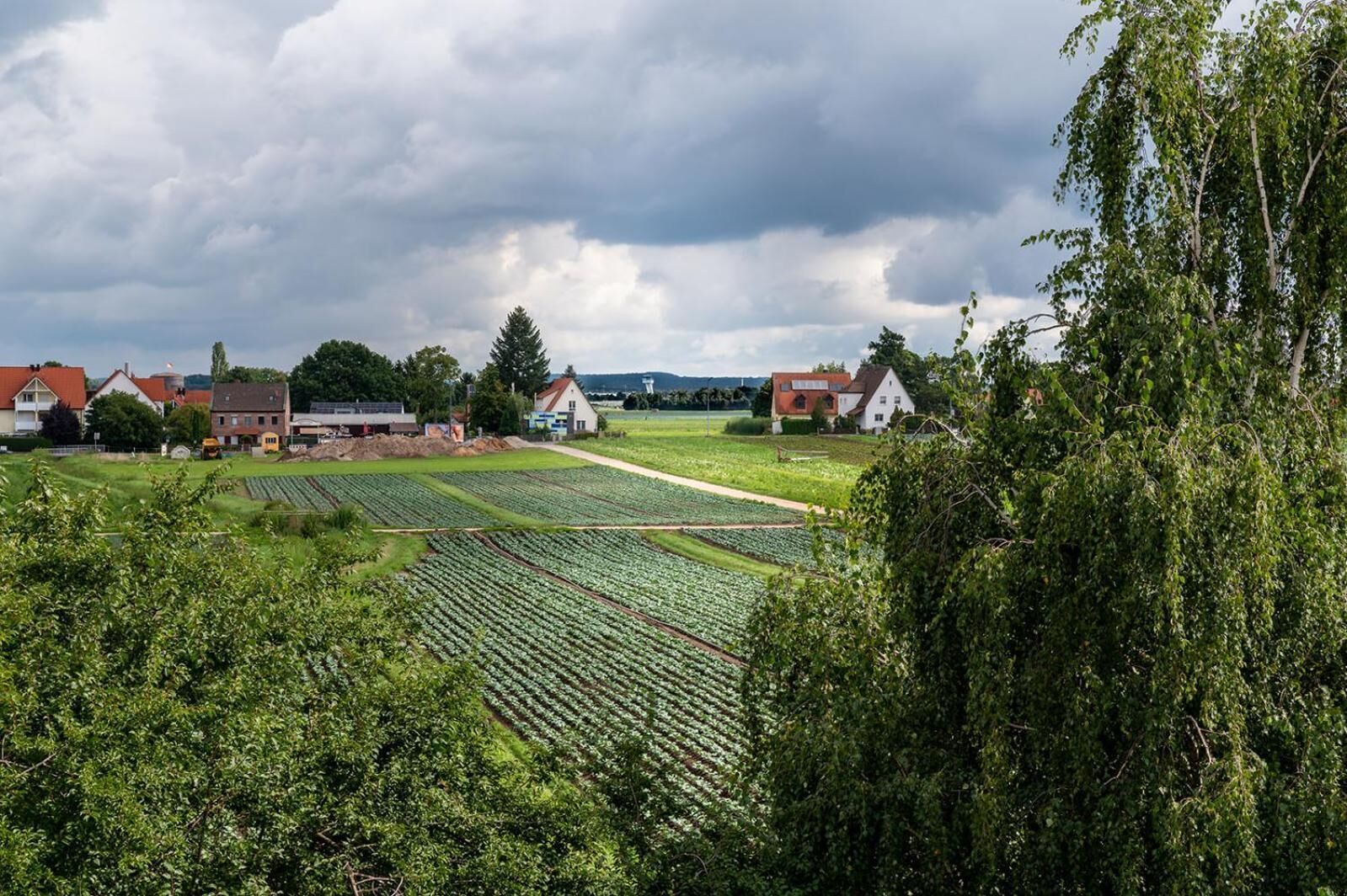 Landskab med landbrugsjord, huse og en overskyet himmel.
