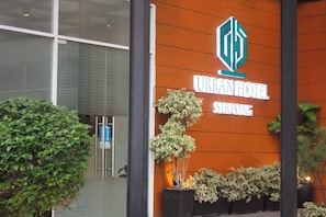 L'esterno dell'HOTEL URBAN SER PONG, caratterizzato da un design moderno con un logo ben visibile, un'ampia pianta in vaso e un ingresso pulito.