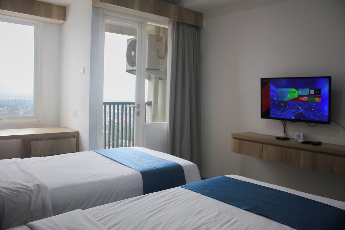 Ein Hotelzimmer mit zwei Betten, einem Fernseher auf einer Holzablage, einem Fenster mit Blick und einer Klimaanlage.