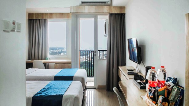A hotel room with two beds, a desk, a television, and a balcony with a view. - Urban Hotel Serpong by Zuzu (South Tangerang)