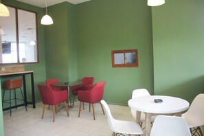Een kamer met groene wanden, een houten tafel en rode en witte stoelen.