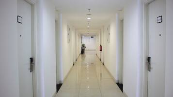 A long, narrow hallway with white walls and doors, leading to a room at the end.
