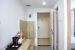 A hallway with a coffee maker, bottled water, and a basket on a counter. A door with a sign is visible in the distance. - Urban Hotel Serpong by Zuzu (South Tangerang)