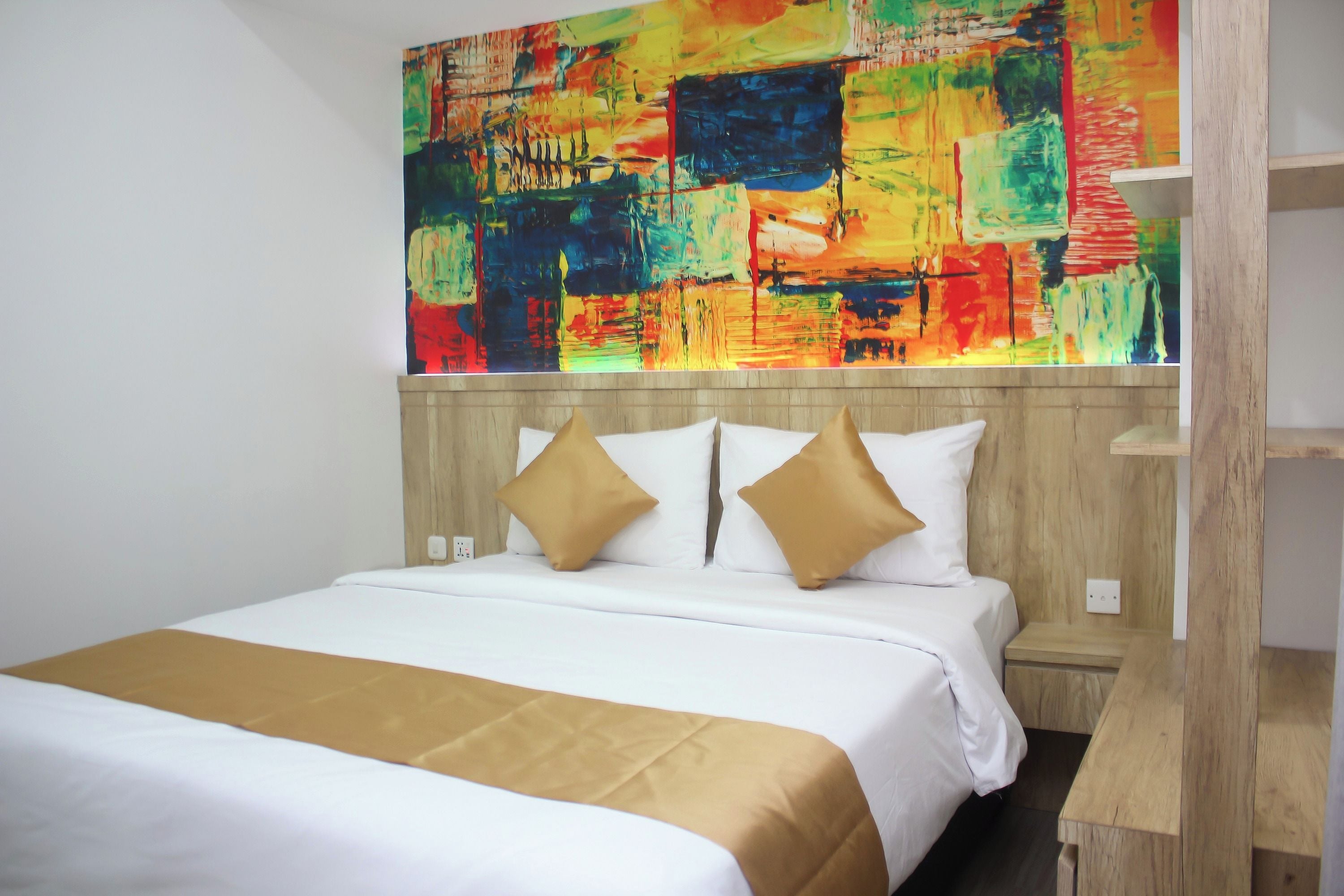A hotel room with a large bed, a wooden headboard, and a colorful abstract painting on the wall.