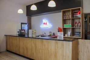 A reception area with a wooden counter, a neon sign for Urban Kitchen, and a shelf with bottled water and flags. - Urban Hotel Serpong by Zuzu (South Tangerang)