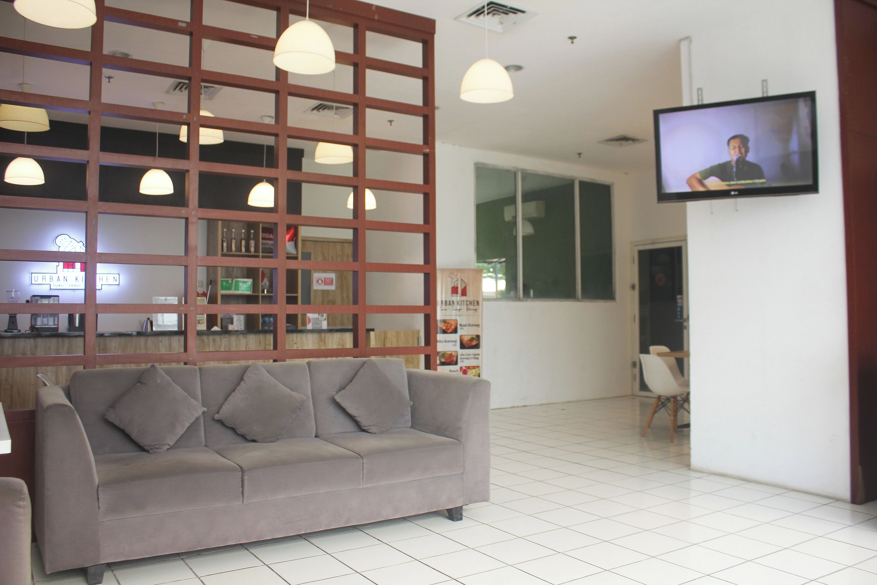 A modern interior with a grey sofa, pendant lights, a TV on the wall, and a reception area with a counter and menu board.