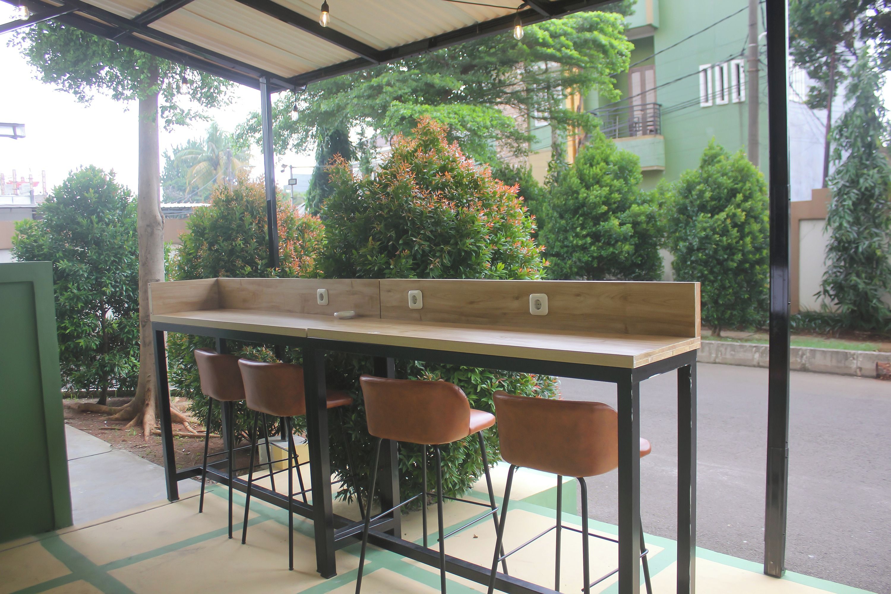 An outdoor seating area with a table and four chairs, surrounded by greenery and a building in the background.