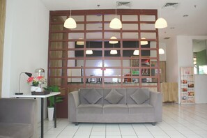 A modern interior with a grey sofa, a small table with a lamp, and a decorative plant. - Urban Hotel Serpong by Zuzu (South Tangerang)
