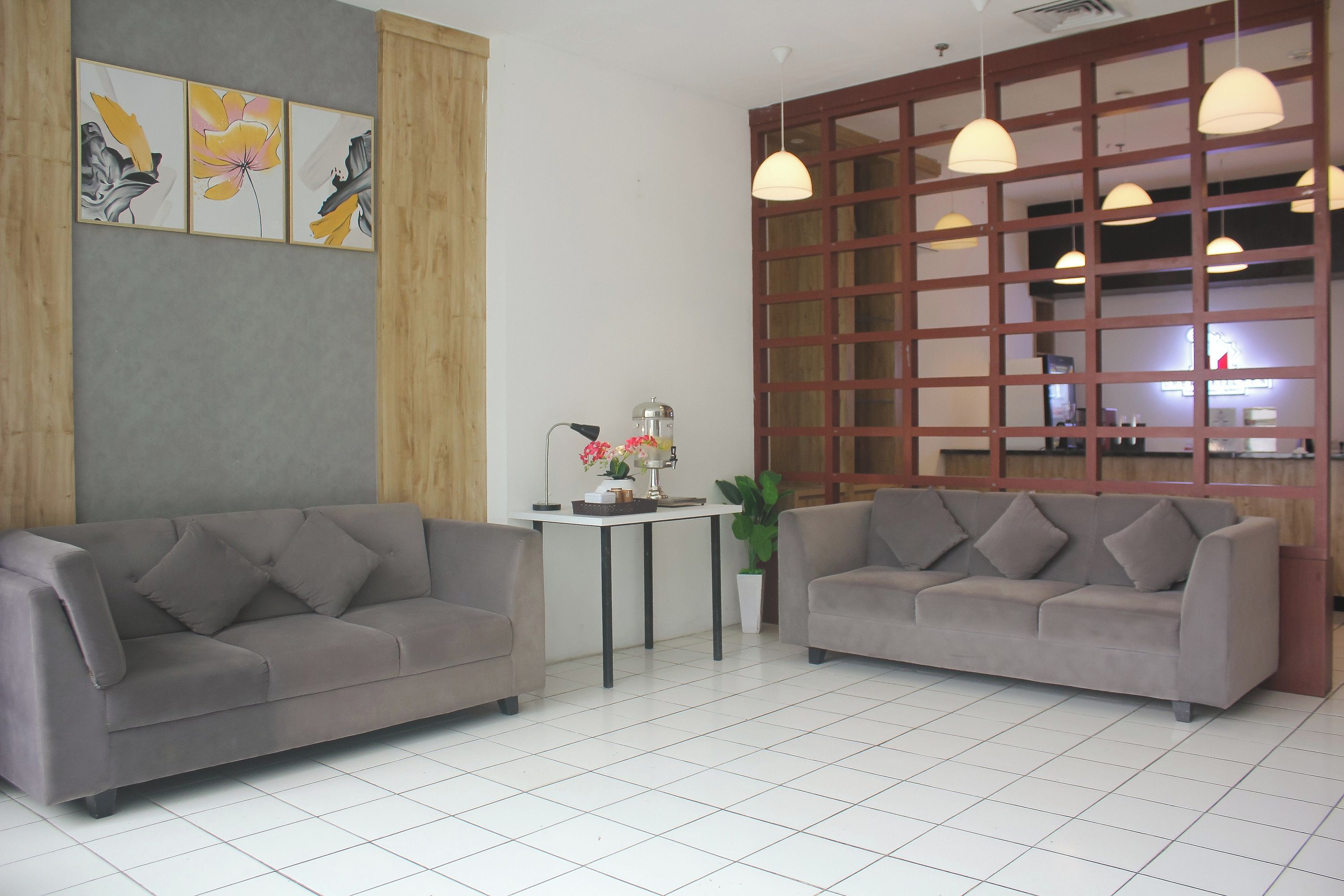 A modern living room with two grey sofas, a small table with a lamp, and a decorative wall with floral artwork.