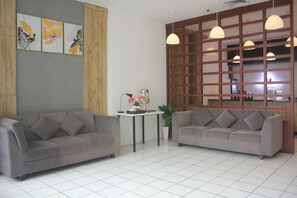 A modern living room with two grey sofas, a small table with a lamp, and a decorative wall with floral artwork. - Urban Hotel Serpong by Zuzu (South Tangerang)