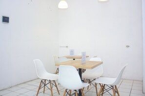 Ein kleiner, sauberer Raum mit einem Holztisch, weißen Stühlen, einer Tafel und einer Uhr an der Wand.