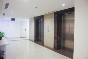 Una hall pulita e moderna con una reception in marmo, una zona accoglienza e due ascensori.