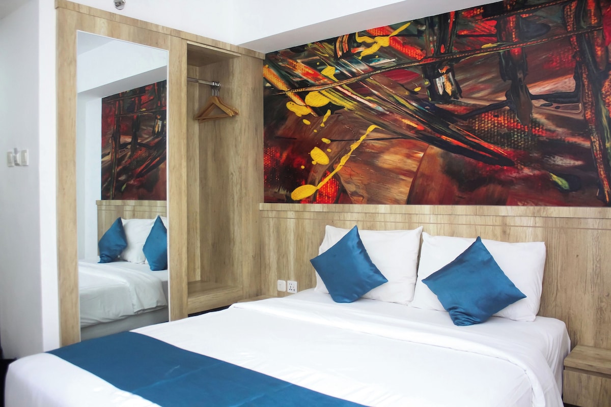 Ein Hotelzimmer mit einem großen Bett, einem Spiegel und einem farbenfrohen abstrakten Gemälde an der Wand.