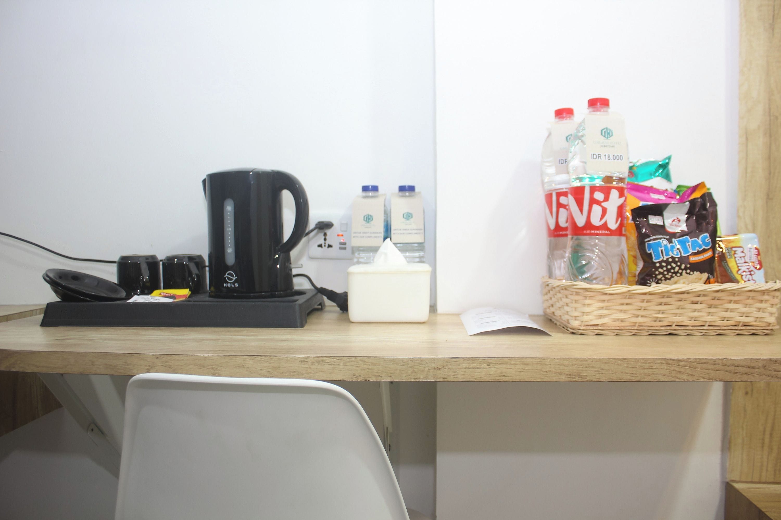 Un escritorio con cafetera, una cesta de aperitivos y agua embotellada.