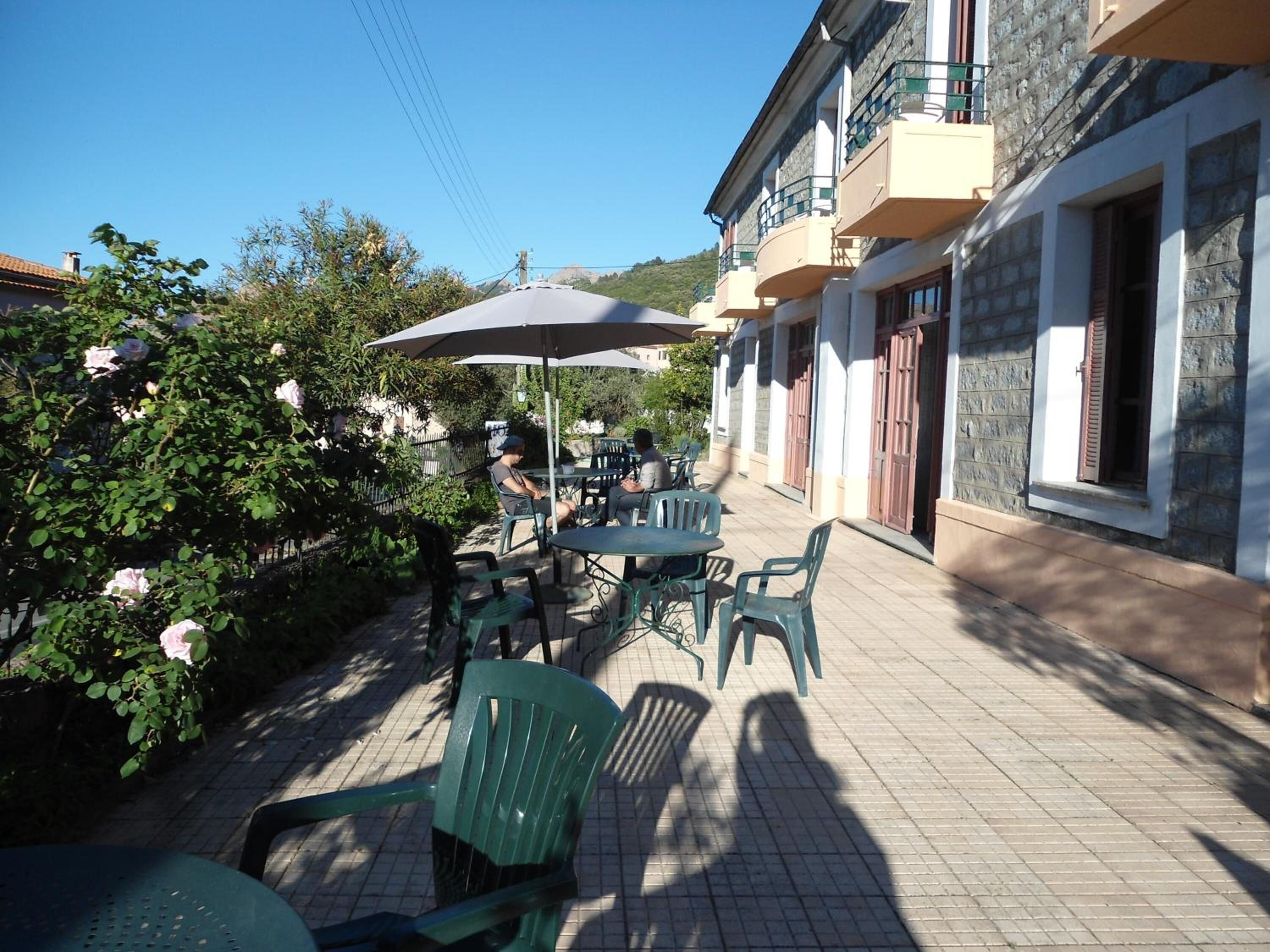 Une terrasse extérieure avec des tables et des chaises, entourée de verdure et bordée d’un immeuble doté de balcons.