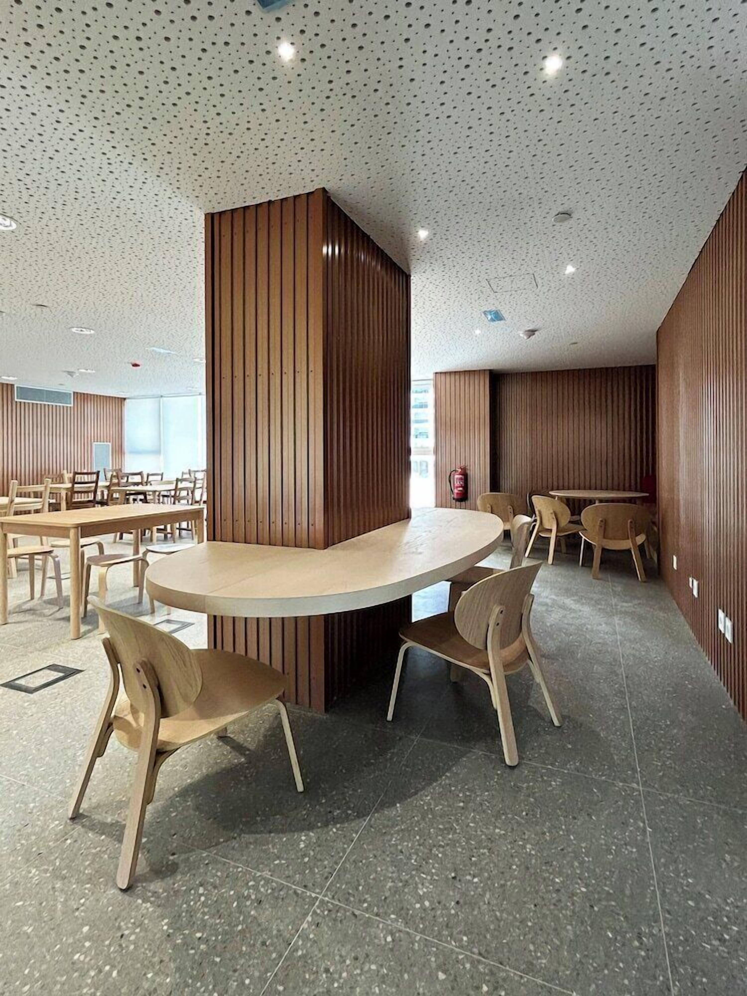 Un interior moderno con una mesa redonda rodeada de sillas, paneles de madera en las paredes y un techo moteado.