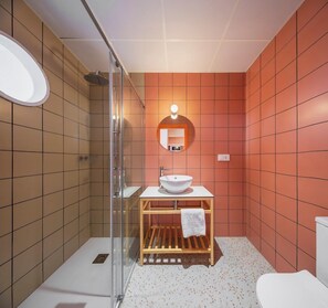 Een moderne badkamer met een douchecabine van glas, een witte wastafel met houten meubel en een ronde spiegel met verlichting.