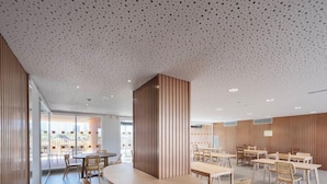 A modern interior with round tables and wooden chairs, a perforated ceiling, and a view through large windows. - Loop Homes Tower Burjassot (Burjasot)