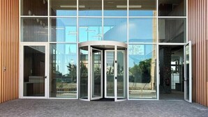 A modern building entrance with large glass doors, a revolving door, and a wooden facade. - Loop Homes Tower Burjassot (Burjasot)
