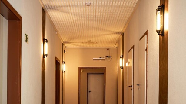 A hallway with wooden flooring, a patterned ceiling, and doors with wall-mounted lights. - Hotel Muhlental (Wernigerode)