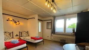A room with two beds, a dining table, and a window with a view of greenery outside. - Hotel Muhlental (Wernigerode)