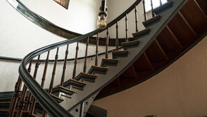 A curved wooden staircase with a metal railing, a ceiling with hanging light fixtures, and a framed picture on the wall. - Hotel Muhlental (Wernigerode)