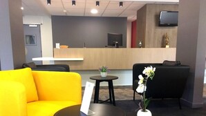 A reception area with a wooden desk, a black sofa, a yellow armchair, and two small tables with vases. - The Originals City, Ara Hotel, Landerneau (Landerneau)