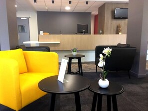 A reception area with a wooden desk, a black sofa, a yellow armchair, and two small tables with vases. - The Originals City, Ara Hotel, Landerneau (Landerneau)